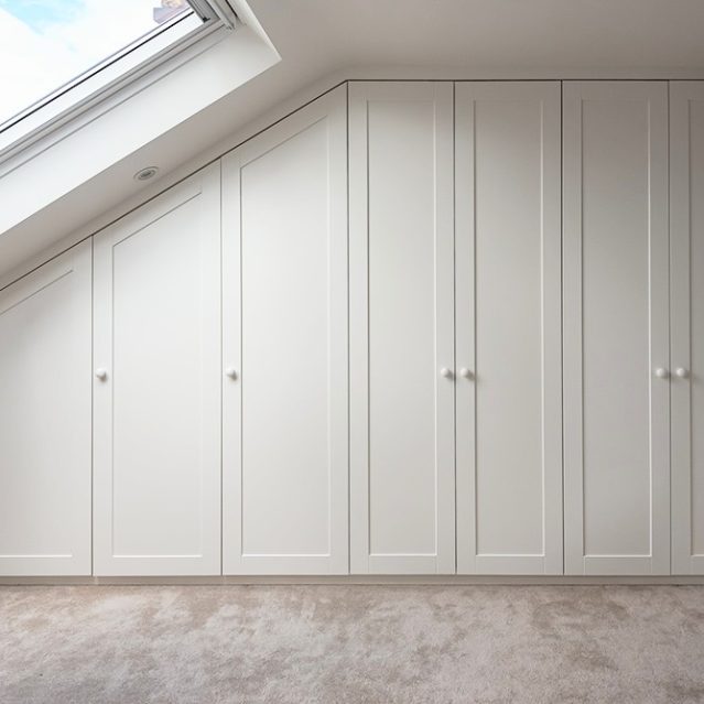 Large wall to wall built-in wardrobe on slanted wall with 8 doors in loft bedroom